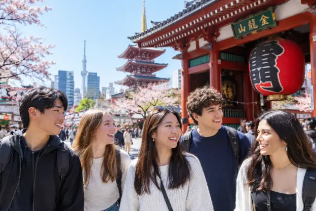 A group of young people exploring Tokyo, with cherry blossoms and temple buildings in the background